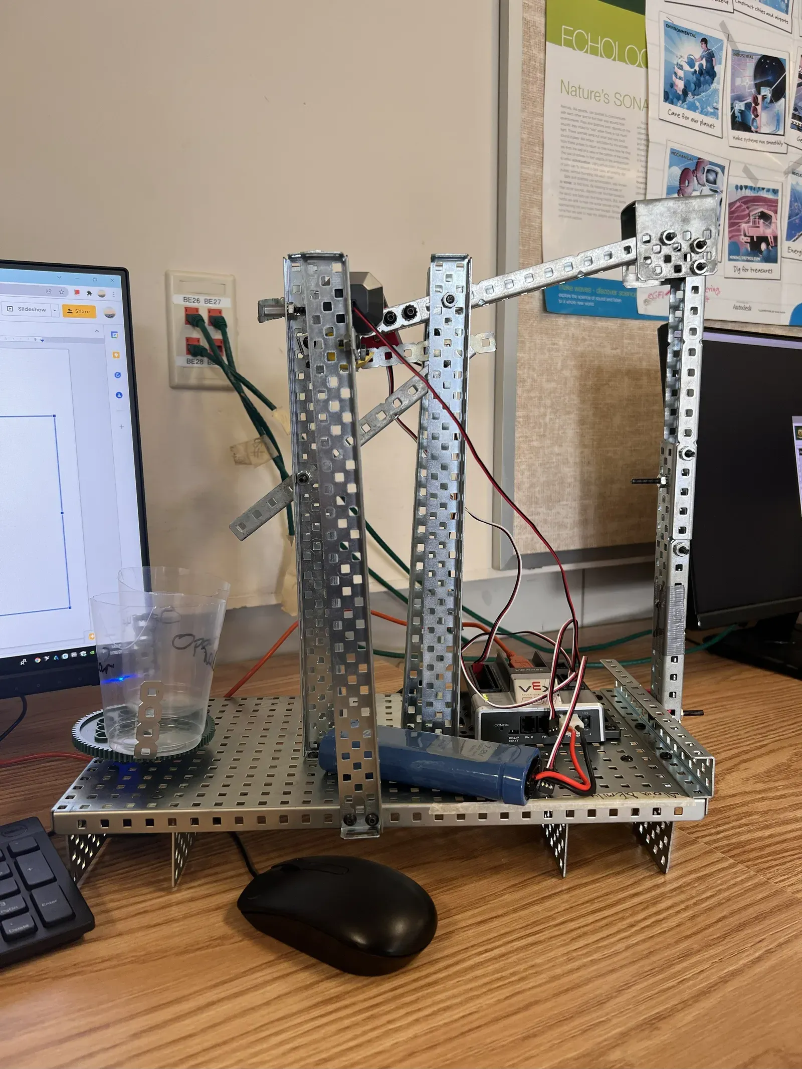 Assembled VEX marble sorter on a classroom desk, with the funnel, light-sensor station, servo-driven diverter, and clear collection cup visible against a classroom bulletin board