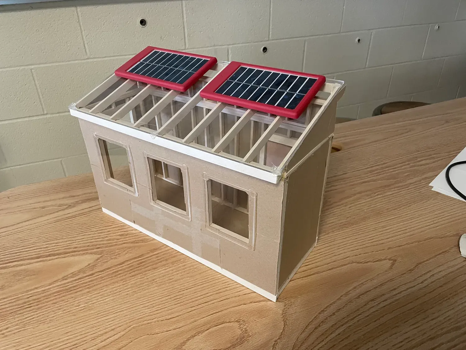 Handmade scale model of the greenhouse with a framed translucent roof and two small red-framed solar panels mounted on top