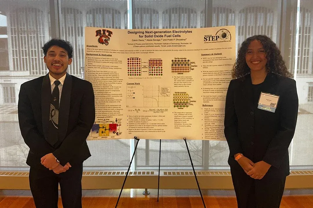 Alexia Savage and Calvin Davis standing on either side of their research poster at a symposium, both in black suits, with the RIT and STEP logos on the poster