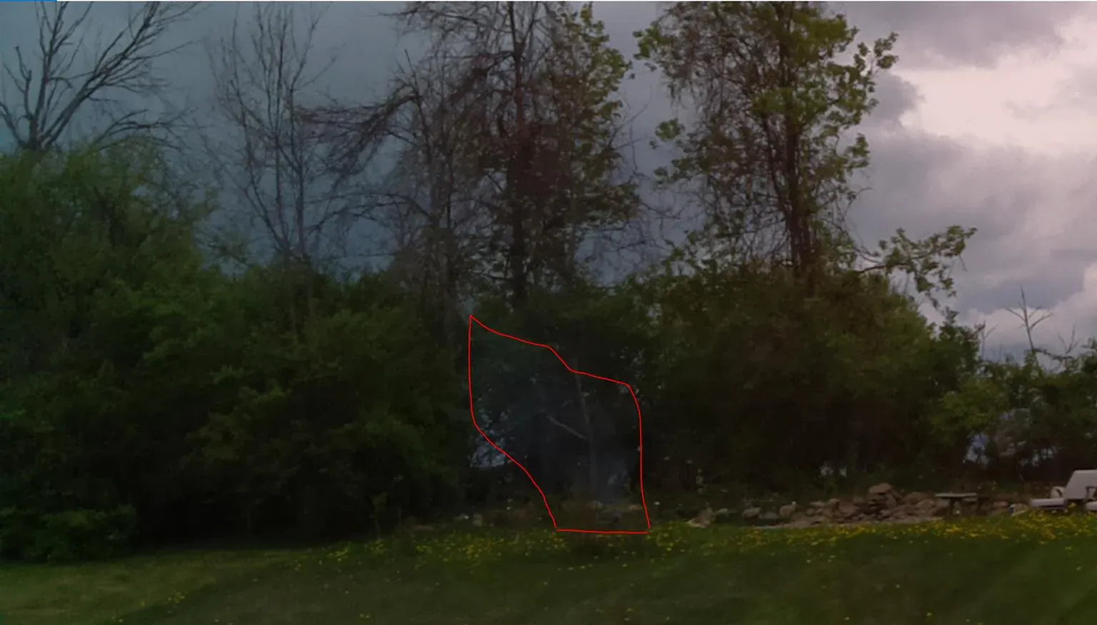 Photo taken by the device's camera across a yard toward a treeline, with a red outline around a faint plume of smoke from a campfire about 80 feet away