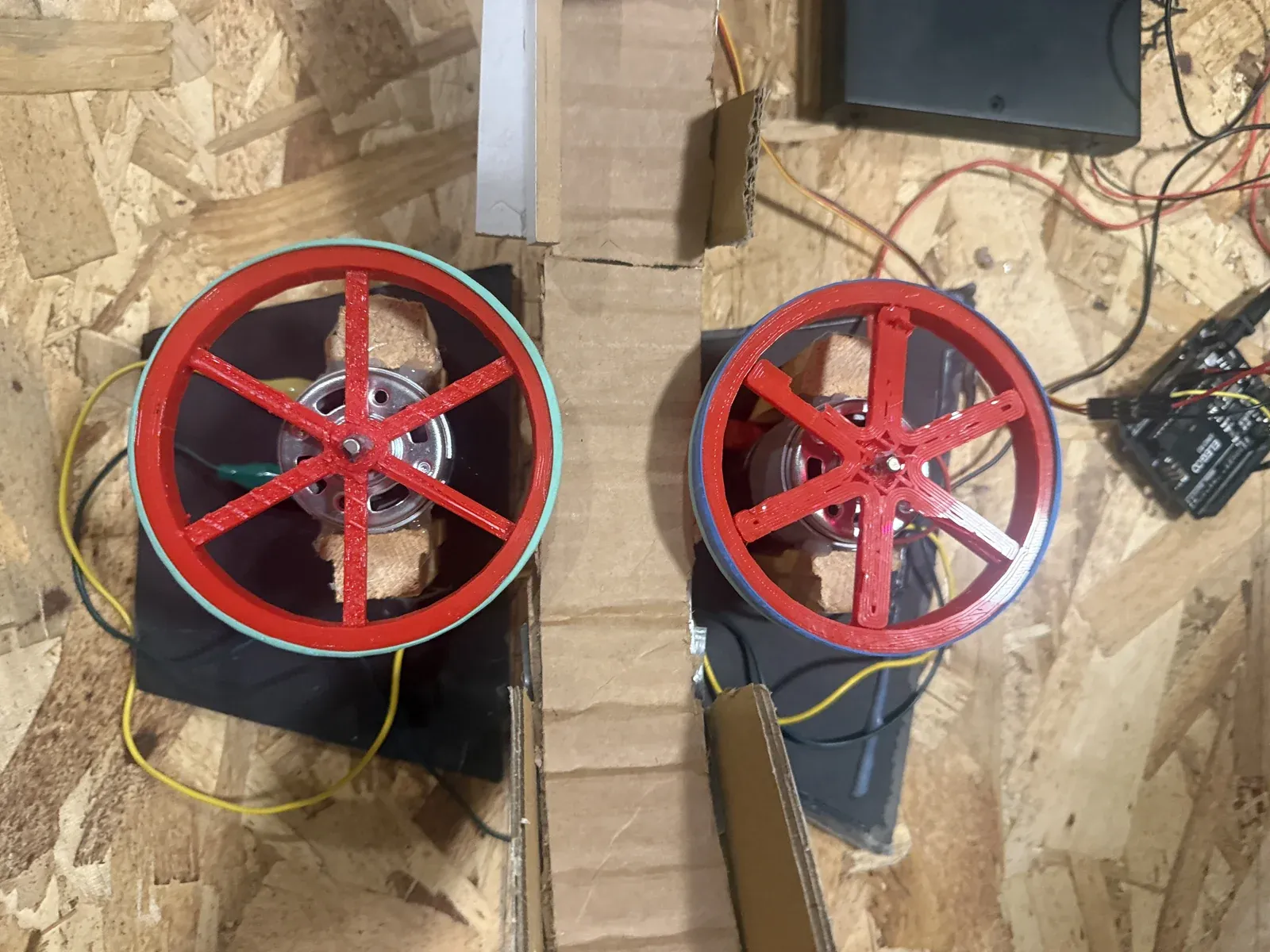 Top-down view of the two red 3D-printed flywheels with rubber bands around their rims, each mounted on a DC motor, with the ramp between them and the Arduino to the side